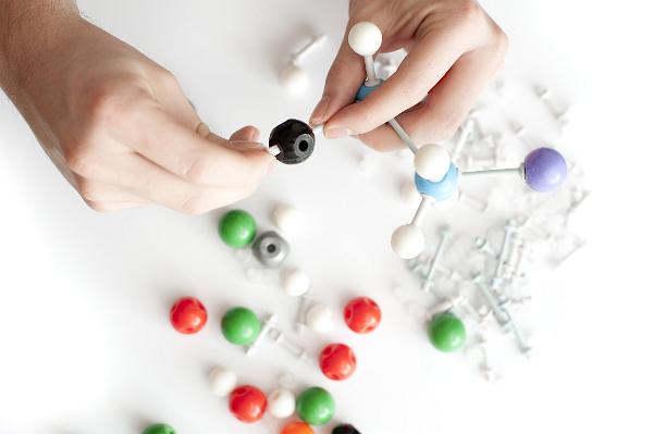 Man constructing a 3d chemistry molecule model from colourful balls and sticks during a demonstration in class in a close up on his hands