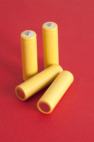 Four unlabeled yellow 6v batteries on a red background with copyspace, two showing the positive and two the negative terminal