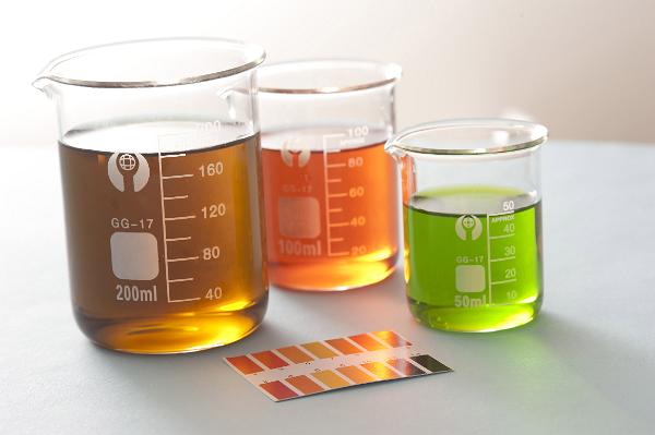Chemistry pH indicator solutions in glass beakers with paper chart showing the change in colours due to alkalinity and acidity