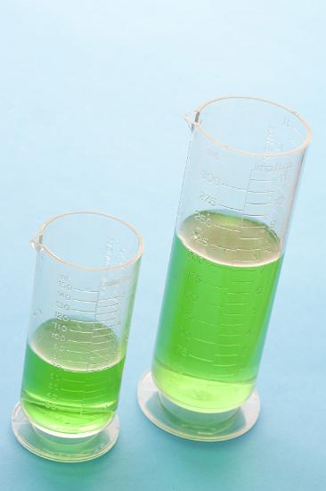 A close up of two measuring beakers filled with green liquid on a blue bench with copy space.