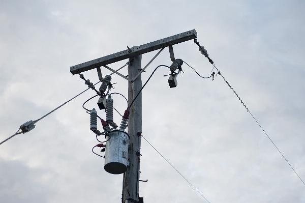 Cylindrical metal transformer mounted at the top on an wooden electricity pole in the distribution and supply network. such a transformer would convert 11kv or 6.6v down to 230 volts to commerical and domestic use