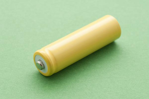 Single yellow unlabelled battery lying diagonally on a green background used to generate electricity from chemical energy