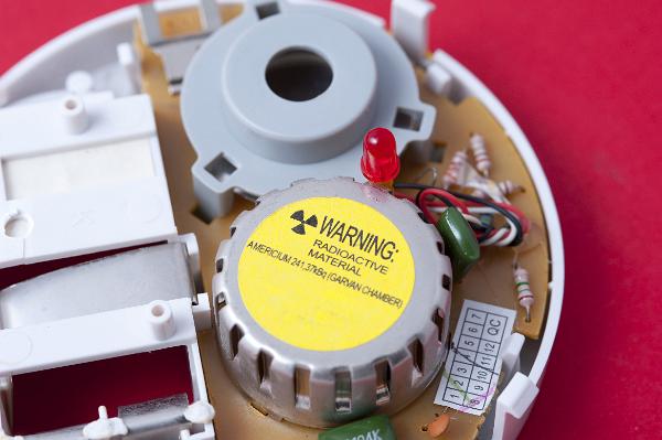 interior of a domestic smoke alarm, the ionizing chamber contains a sealed radioactive source, when smoke enters the chamber the smoke particles absorb some of the radiation from the radioactive course, this drop in emission is detected by a sensor and sounds the alarm