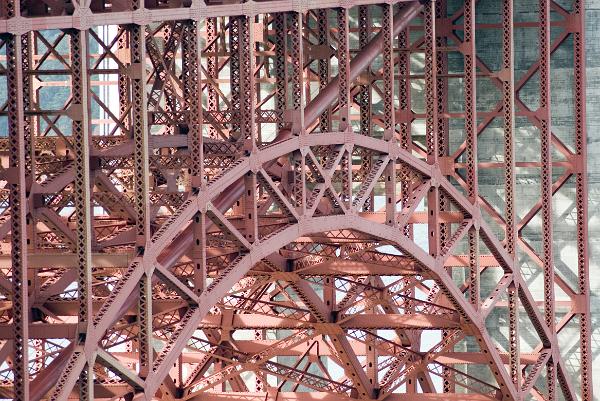details of the steel arch bridge structure at the southern end of the golden gate bridge, metal box trusses form an arch to distribute the load while the main suspension cable passes inbetween from borrom left to top right