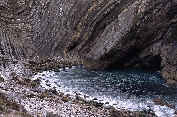 Bay on the Jurassic coast, England showing the folded rock strata in the cliffs exposed by weathering and the accumulation of rock fragments on the beach below which are rich in fossils