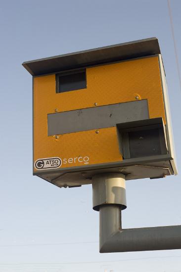 Yellow speed camera mounted on a pole overlooking a road to clock and photograph speeding motorists as they drive by in their cars, the camera uses a radar system the detect the speed of the motorist