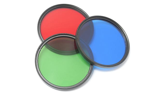 Three circular glass filters with additive colors of red, green and blue arranged to overlap on a white background