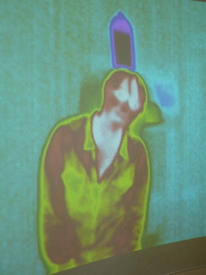 image of a person standing infront of an infra-red thermal imaging camera, white areas are the hotest, black and blue coulours are coller