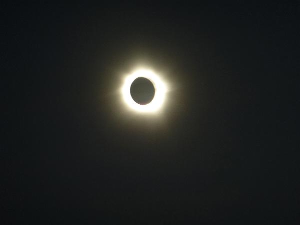 Solar eclipse in a darkened sky with the corona of the sun shining out around the moon as a bright halo