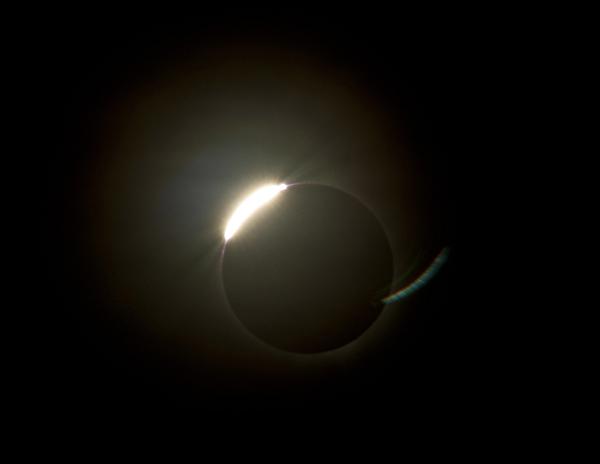 The sun emerging from behind the moon during a total solar eclipse with a ring of illumnated corona still visible