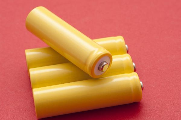 Four unlabeled 1.5v yellow batteries or cells with one balanced across the top showing the positive terminal on a red background