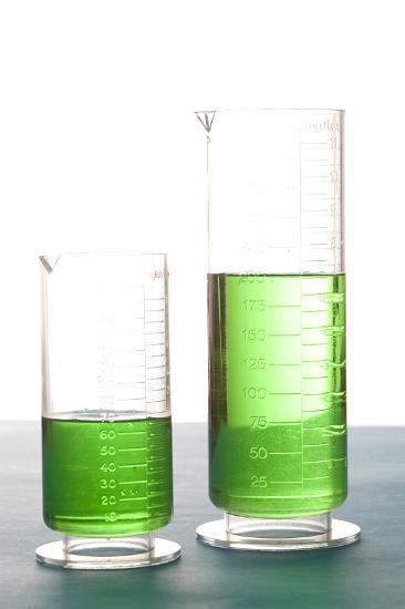 Two measuring cylinders in a chemistry laboratory filled to different levels with green liquid measuring the volumes