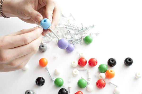 A close up of a person putting together a plastic molecular model on a white background with copy space.
