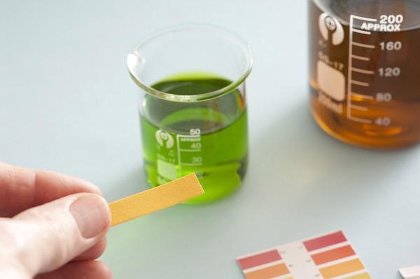 Beakers with a green universal indicator solution and yellow litmus paper showing a neutral pH during testing in a laboratory