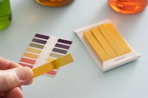 PH litmus paper test after being used with color sampler and several glasses with liquid examples in background. Chemistry class concept