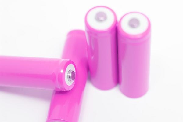 Four unlabeled pink batteries or primary cells to generate electricity on a white background with focus to one positive terminal