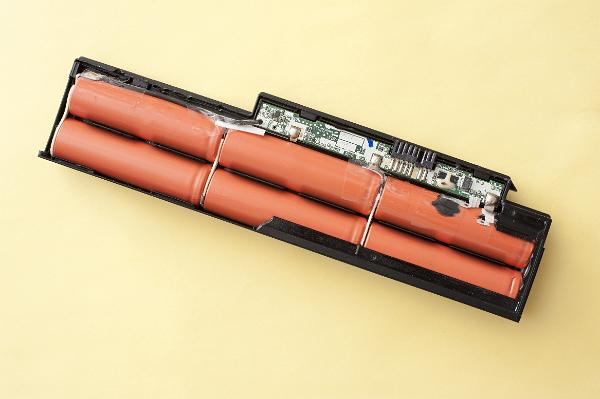 Disassembled laptop battery with six lithium ion elements and electronic circuit inside, viewed from above on yellow background